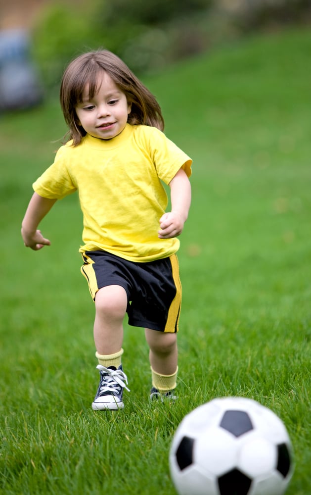 happy kid playing football in a park outdoors
