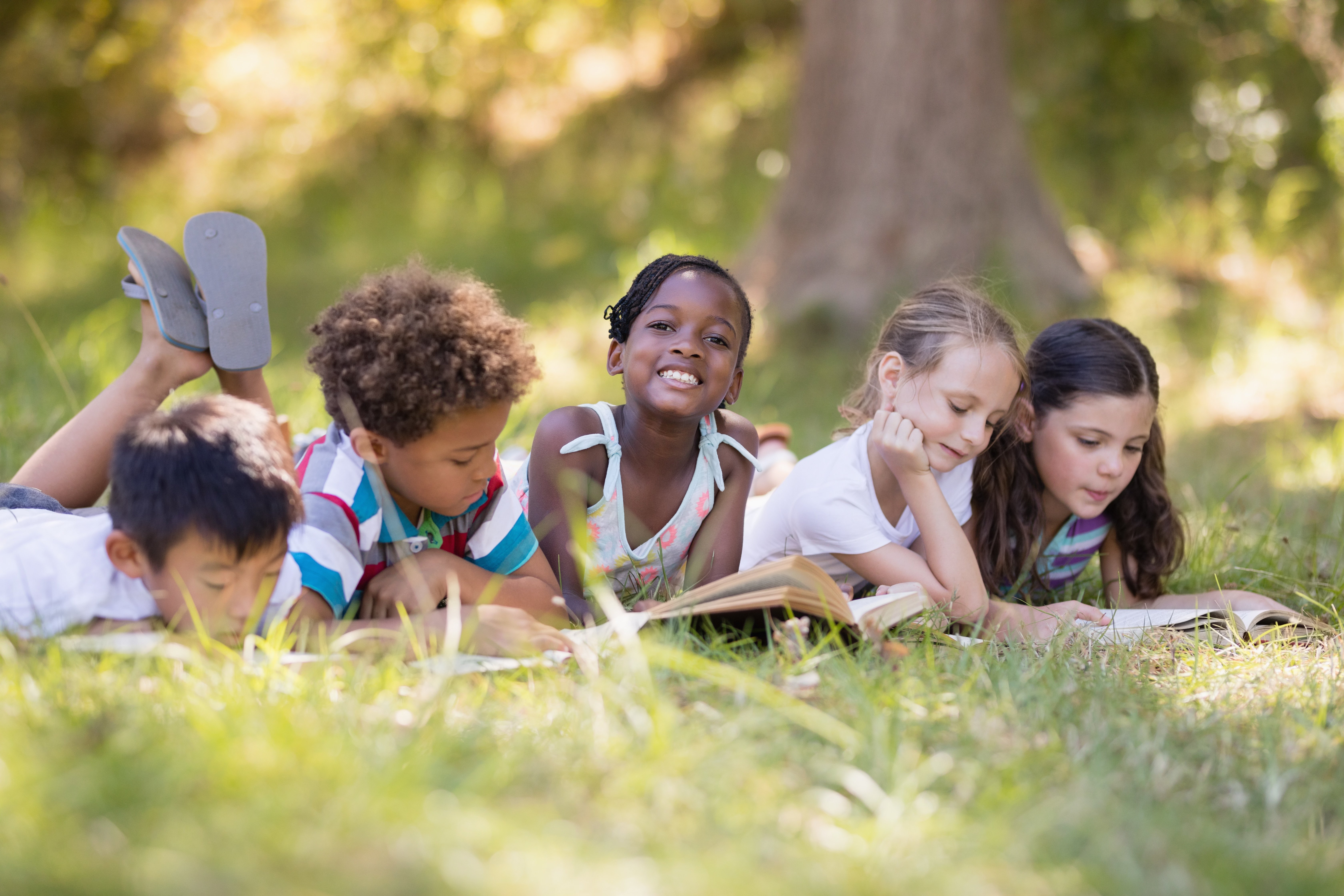 five kids laying in the grass reading books at summer camp