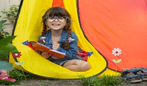 little girl with glases sitting in a tent reading a book in the grass