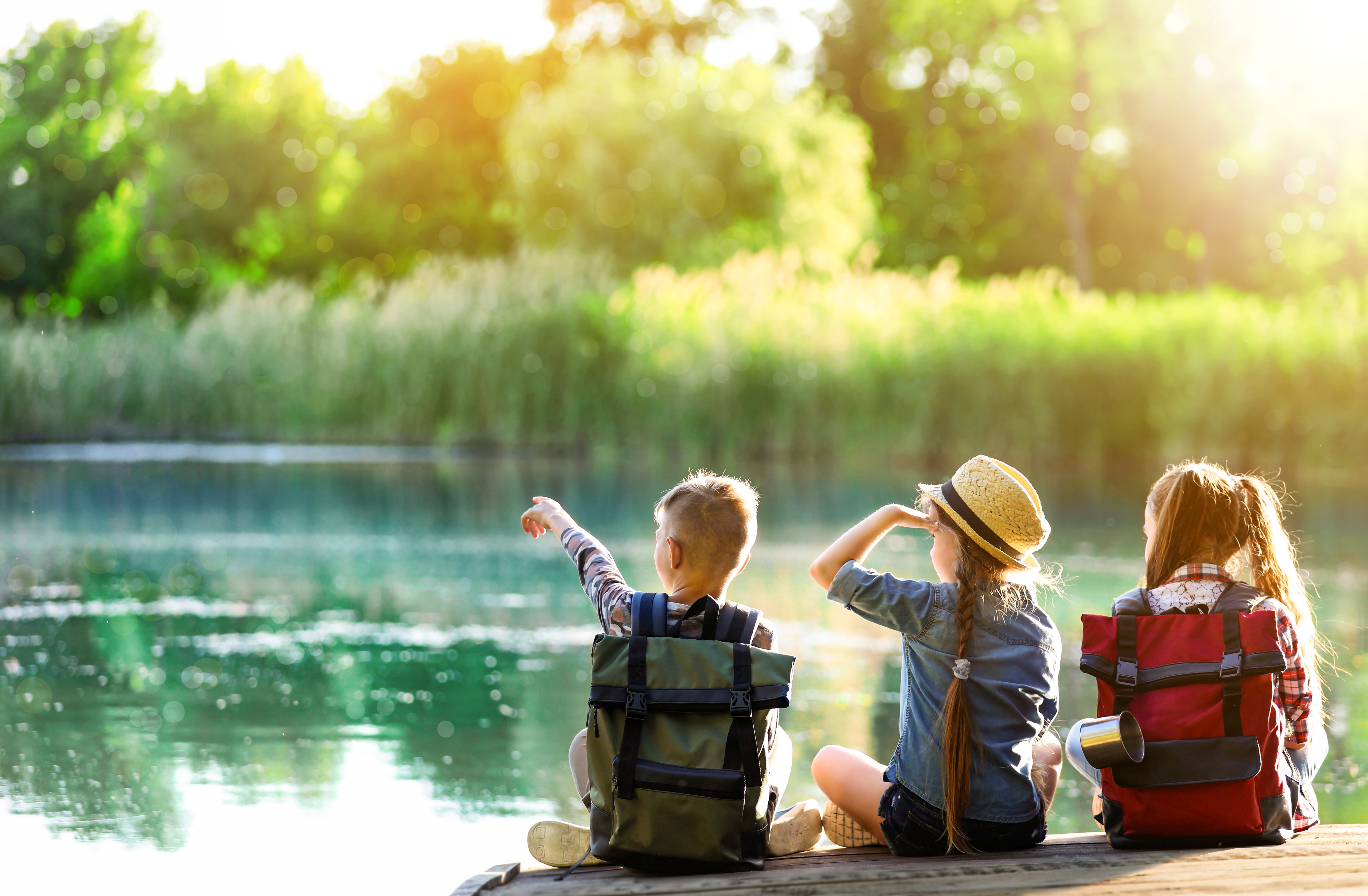 3 kids sitting on a lake surrounded by shrubbery
