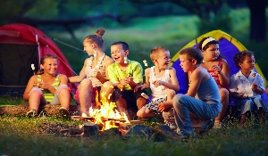 boys and girls gathered around a campfire roasting s'mores