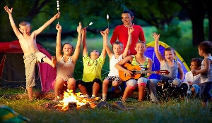 kids gathered around a campfire with counselor playing music and roasting s'mores