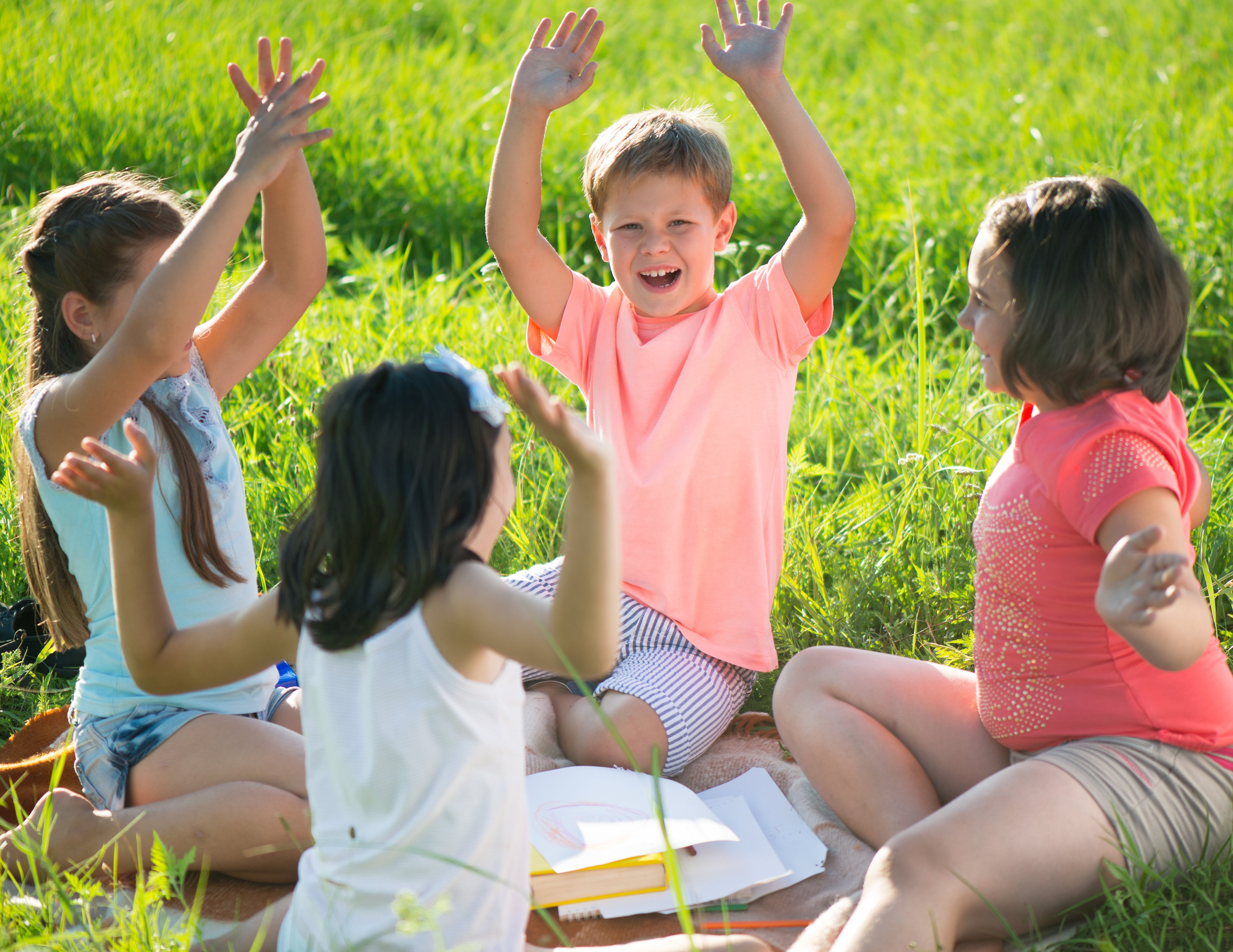 four kids sitting in a grass field playing a game with their hands in the air